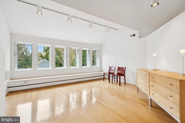 living area featuring rail lighting, a healthy amount of sunlight, lofted ceiling, and a baseboard radiator