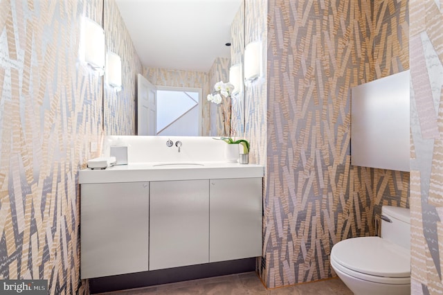 bathroom with toilet, wallpapered walls, and vanity