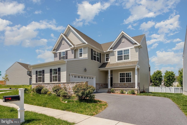 craftsman inspired home featuring board and batten siding, fence, aphalt driveway, an attached garage, and stone siding