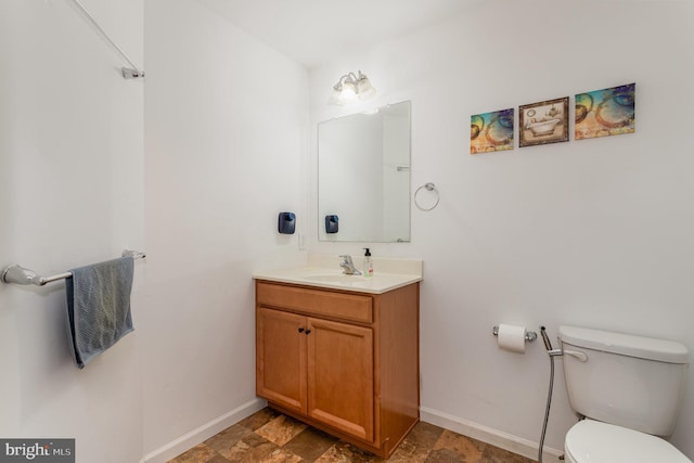 bathroom with baseboards, stone finish flooring, toilet, and vanity