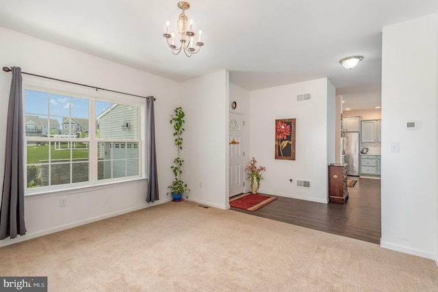 spare room featuring carpet floors, baseboards, a chandelier, and visible vents