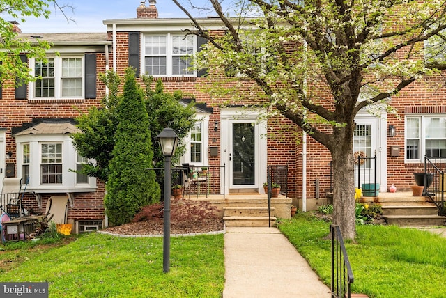 view of property featuring brick siding, a chimney, and a front lawn