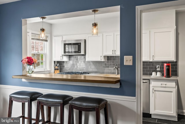 kitchen with a sink, wood counters, appliances with stainless steel finishes, and white cabinetry