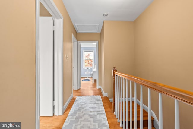 corridor featuring baseboards, an upstairs landing, attic access, and light wood-type flooring