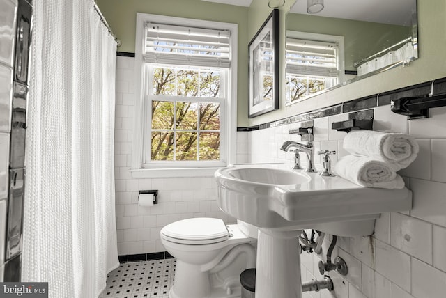 full bathroom with a wealth of natural light, toilet, and tile walls