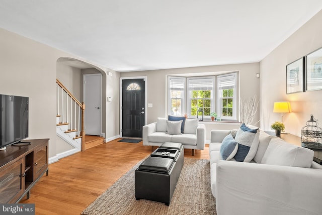 living area with stairway, arched walkways, baseboards, and light wood-style flooring