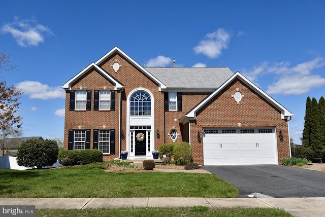 colonial inspired home featuring a front yard, brick siding, a garage, and aphalt driveway