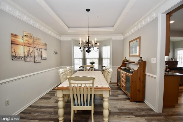dining space with ornamental molding, an inviting chandelier, dark wood-style flooring, and a raised ceiling