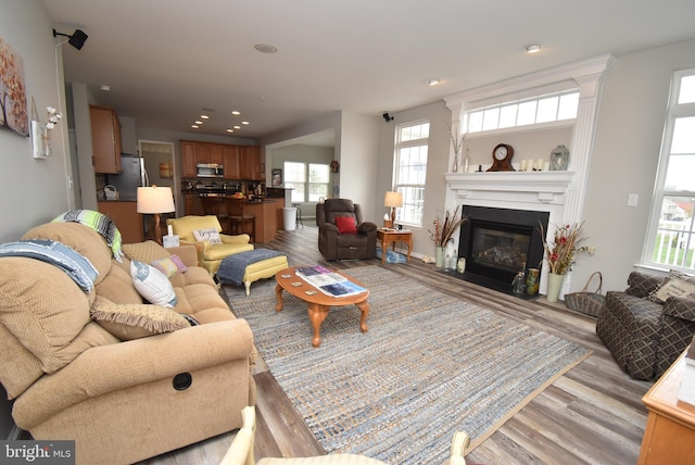 living area featuring a fireplace with flush hearth, light wood-style floors, plenty of natural light, and recessed lighting
