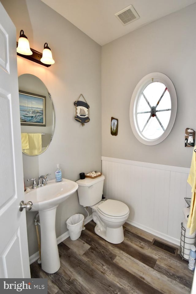 half bathroom with visible vents, wood finished floors, a wainscoted wall, and toilet