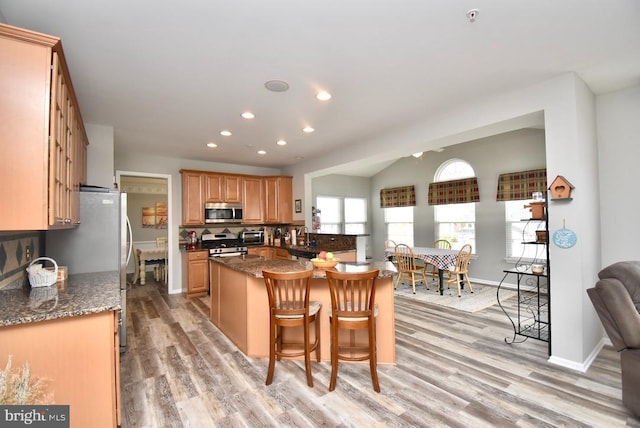 kitchen featuring dark stone counters, light wood-style flooring, a breakfast bar, stainless steel appliances, and recessed lighting