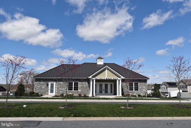 view of front of house with a standing seam roof, a front lawn, metal roof, stone siding, and french doors
