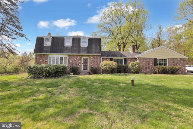 colonial inspired home with a chimney, brick siding, a shingled roof, and a front yard