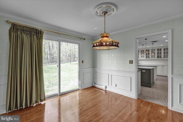 unfurnished dining area with light wood-style floors, ornamental molding, a baseboard heating unit, and wainscoting
