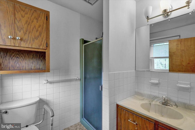 bathroom featuring tile walls, vanity, toilet, a stall shower, and wainscoting