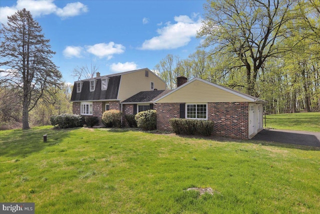 colonial inspired home featuring a front yard, a gambrel roof, a garage, a chimney, and brick siding