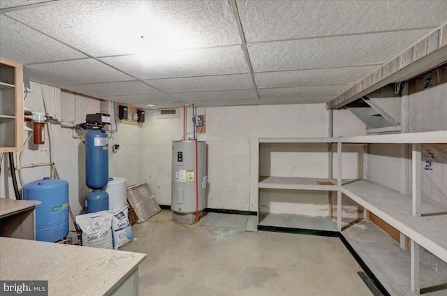 unfinished below grade area featuring water heater, concrete block wall, and a drop ceiling