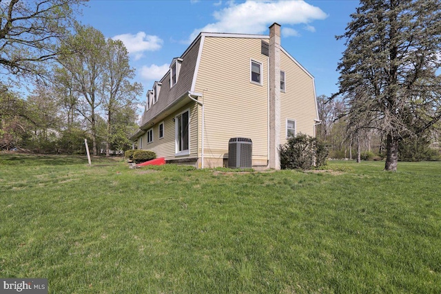 view of home's exterior with cooling unit, a lawn, a gambrel roof, and a chimney