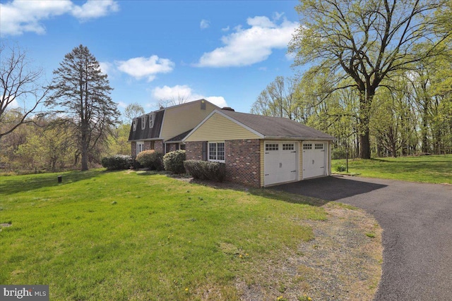 view of property exterior with brick siding, aphalt driveway, a lawn, a chimney, and an attached garage