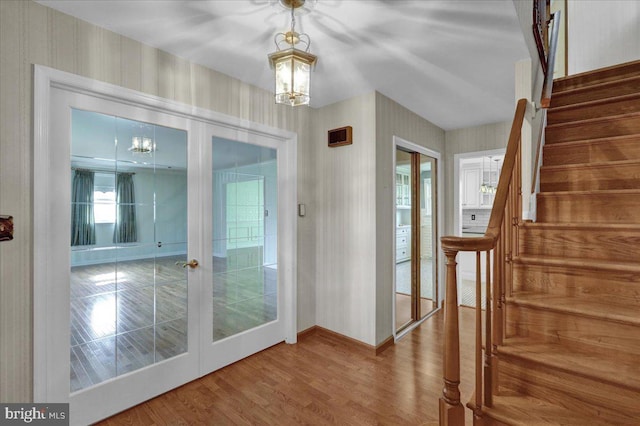 doorway featuring french doors, baseboards, wood finished floors, a notable chandelier, and stairs