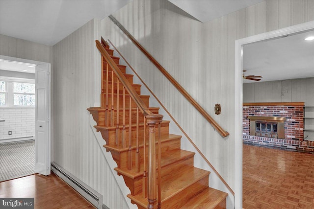stairway featuring wallpapered walls, a baseboard heating unit, a fireplace, and ceiling fan