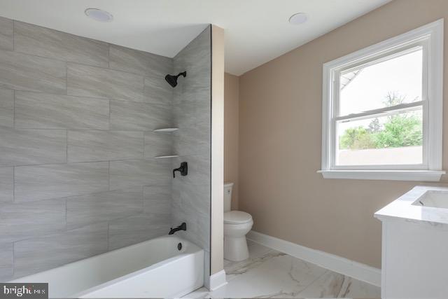 bathroom with washtub / shower combination, vanity, toilet, marble finish floor, and baseboards