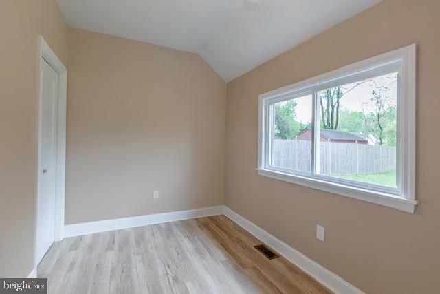 unfurnished room featuring baseboards, visible vents, light wood-style flooring, and lofted ceiling