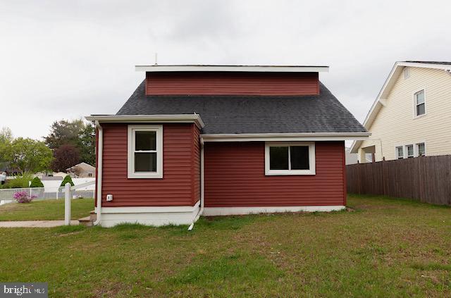 back of house featuring a yard, fence, and roof with shingles
