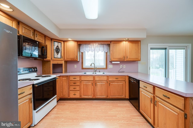 kitchen with a peninsula, light countertops, a sink, light wood finished floors, and black appliances