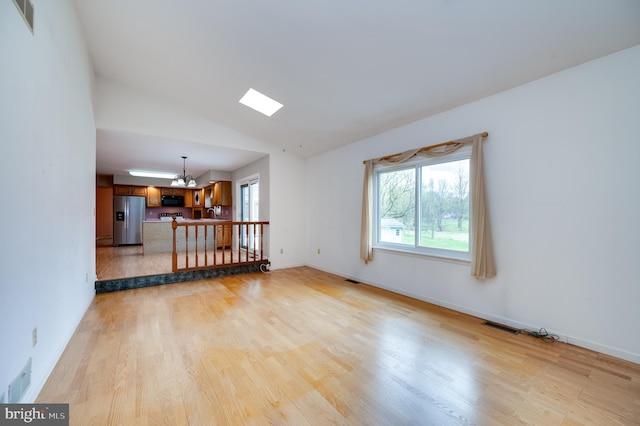 empty room with a chandelier, visible vents, vaulted ceiling, and light wood-type flooring