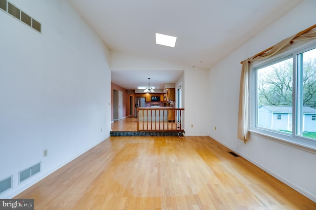 unfurnished living room with visible vents, wood finished floors, a notable chandelier, and vaulted ceiling