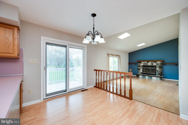 dining room featuring a fireplace, vaulted ceiling, baseboards, light wood finished floors, and an inviting chandelier