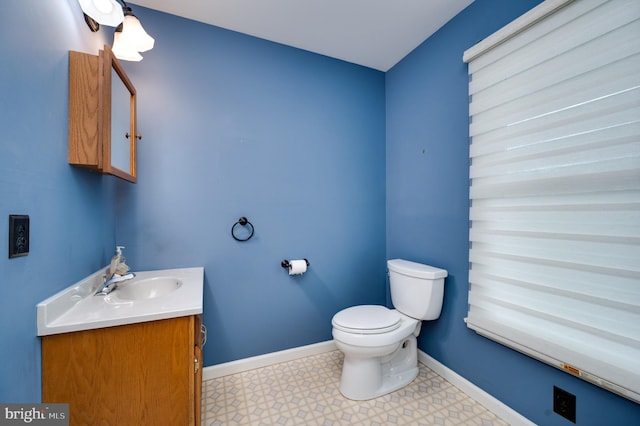 half bathroom featuring toilet, baseboards, and vanity