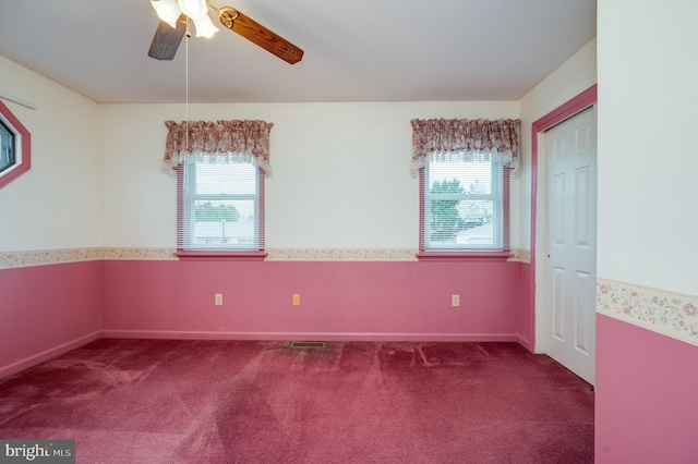carpeted empty room with baseboards, ceiling fan, a wealth of natural light, and visible vents