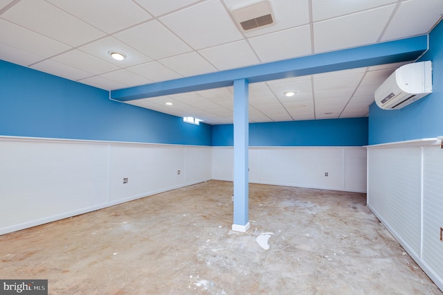 finished below grade area with visible vents, wainscoting, a wall mounted air conditioner, and a paneled ceiling