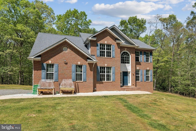colonial inspired home featuring a shingled roof, a front yard, and brick siding