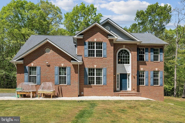 colonial-style house featuring brick siding, a shingled roof, and a front yard