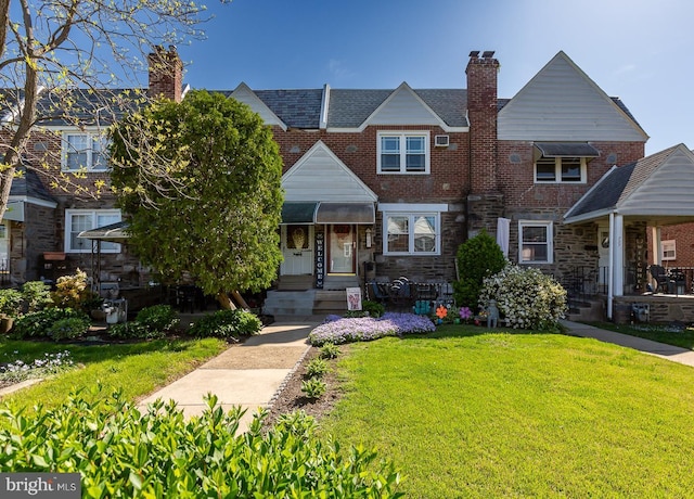 townhome / multi-family property featuring stone siding, brick siding, a chimney, and a front yard
