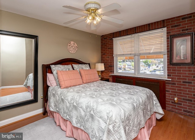bedroom featuring baseboards, ceiling fan, wood finished floors, and brick wall