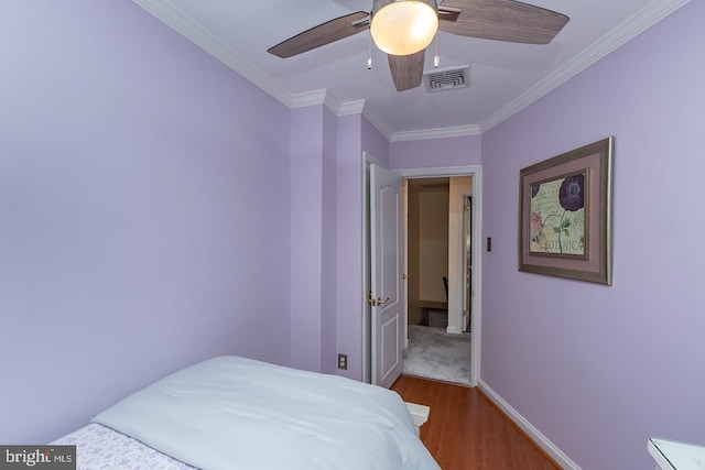bedroom with a ceiling fan, visible vents, crown molding, wood finished floors, and baseboards