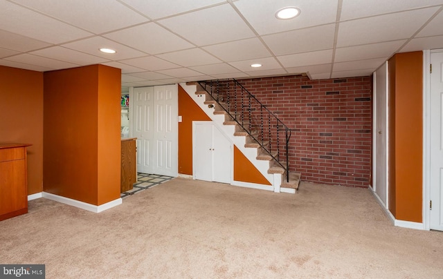finished basement featuring carpet, brick wall, and a paneled ceiling