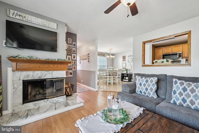 living area with baseboards, ceiling fan with notable chandelier, wood finished floors, and a premium fireplace