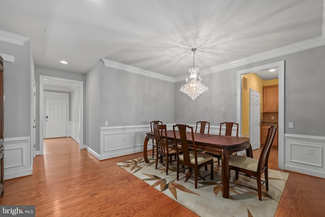 dining room featuring crown molding, wainscoting, a decorative wall, a chandelier, and light wood-style flooring