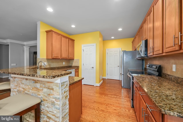 kitchen with a peninsula, a breakfast bar, baseboards, light wood-style floors, and stainless steel appliances