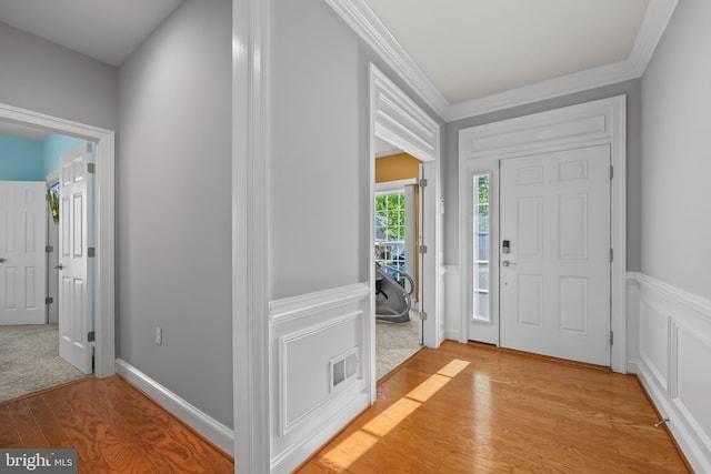 foyer with crown molding, visible vents, light wood-style flooring, and a wainscoted wall