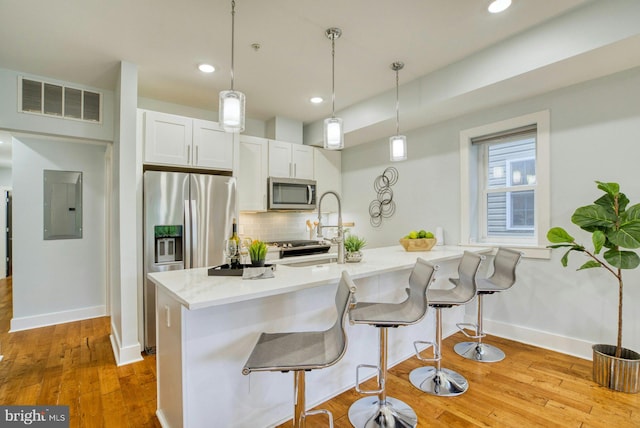 kitchen featuring appliances with stainless steel finishes, electric panel, backsplash, a breakfast bar area, and baseboards