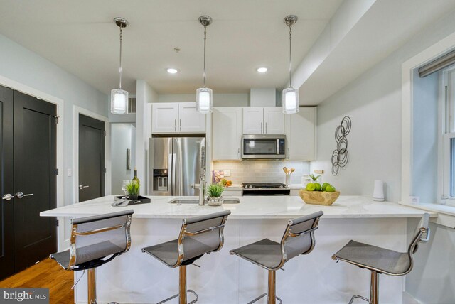 kitchen with appliances with stainless steel finishes, a sink, backsplash, white cabinets, and light stone counters