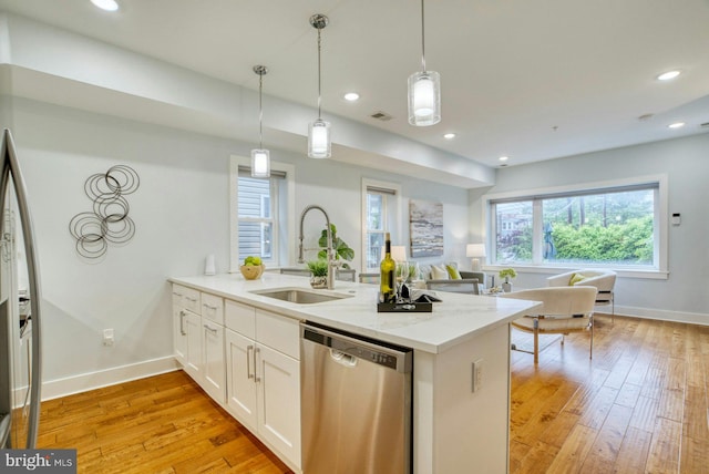 kitchen featuring stainless steel dishwasher, a sink, a peninsula, white cabinets, and light wood-type flooring