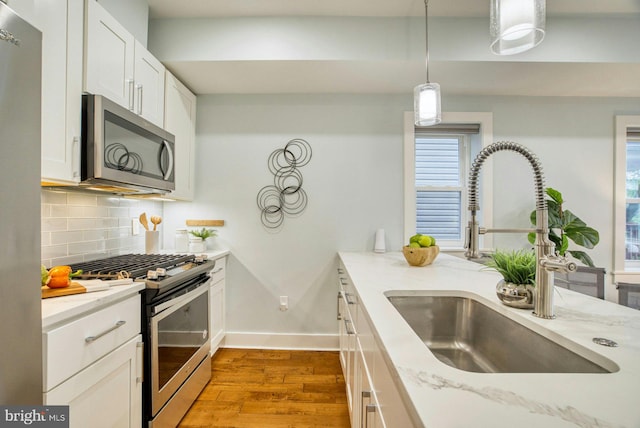 kitchen featuring stainless steel appliances, a sink, wood finished floors, backsplash, and light stone counters