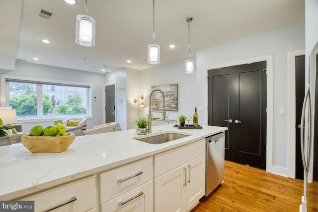 kitchen featuring a sink, dishwasher, light wood-style floors, white cabinetry, and light stone counters